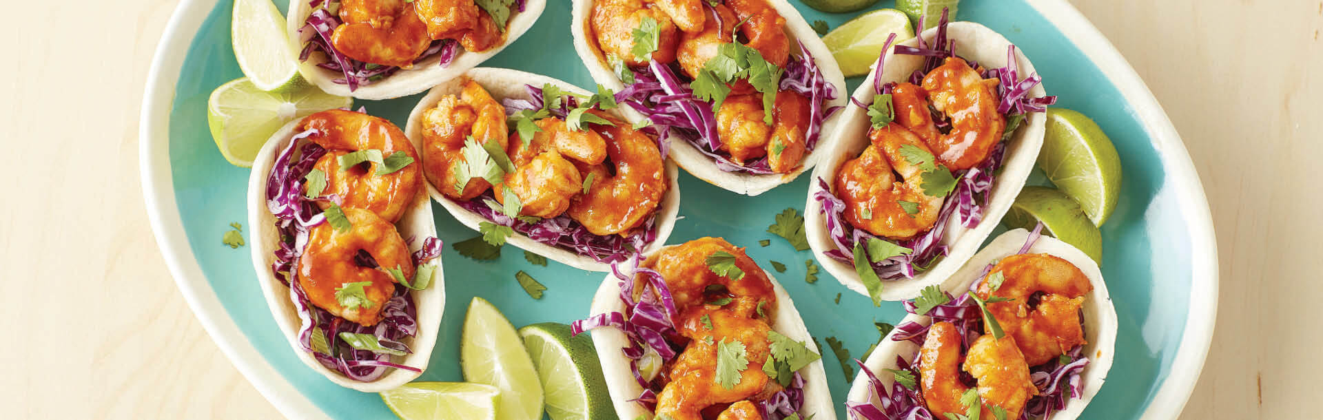 barchette di taco ripiene di gamberi e cavolo tritato servite su un piatto con lime